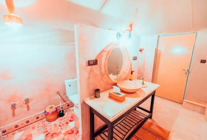 Bagno privato dentro la tenda, con WC, zona doccia e lavabo in pietra con specchio rotondo