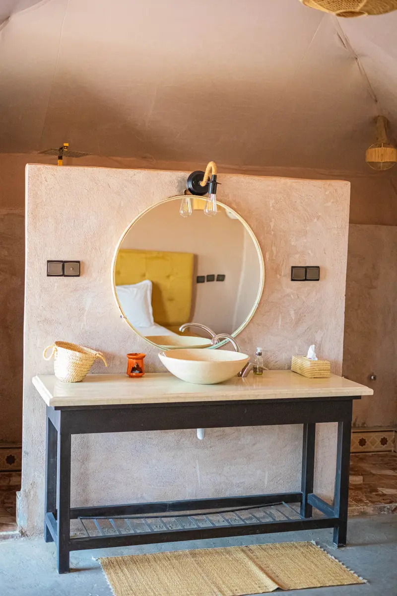 Private bathroom in the tent, with a stone basin, round mirror and toiletries