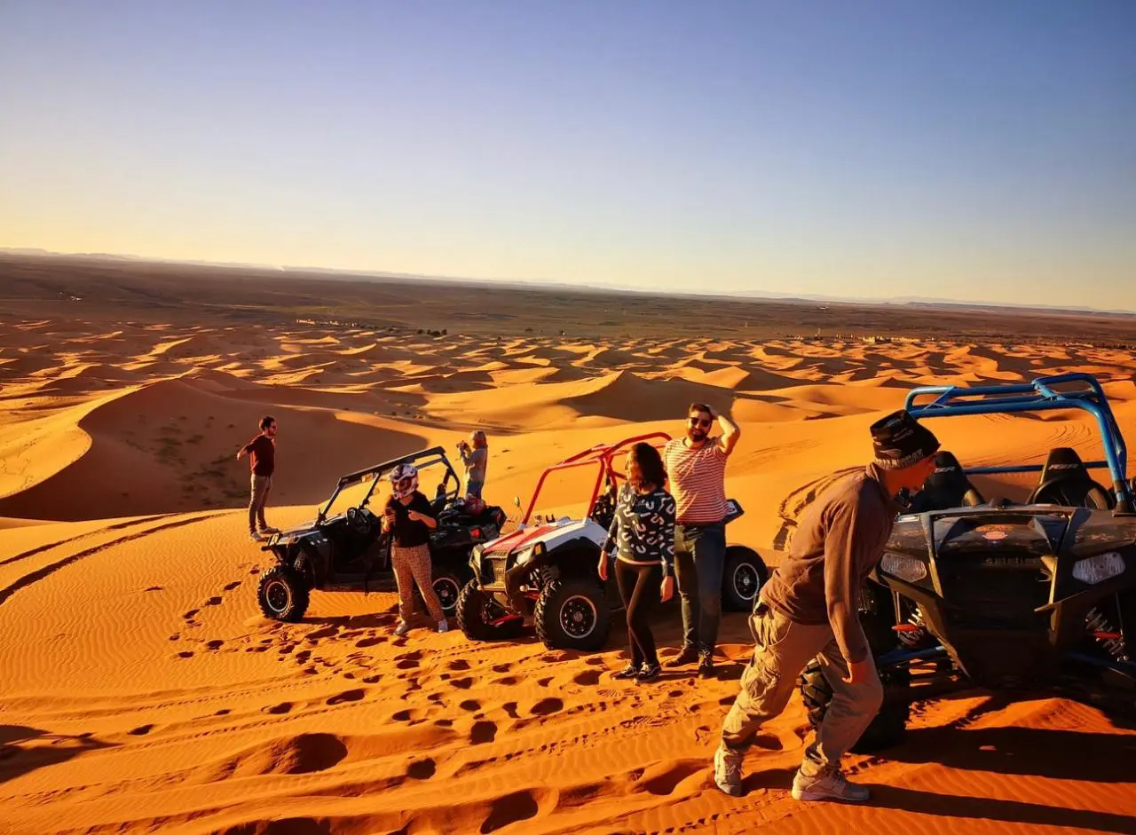 Un groupe d’hôtes avec leurs buggys arrêtés en haut des dunes de Merzouga au coucher du soleil