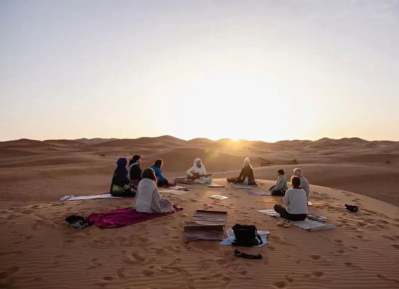 Un groupe pratiquant le yoga en cercle sur les dunes de Merzouga au lever du soleil