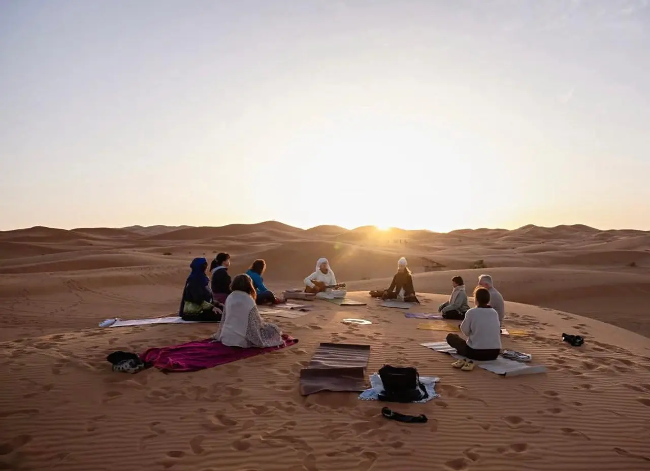 Un groupe pratiquant le yoga en cercle sur les dunes de Merzouga au lever du soleil
