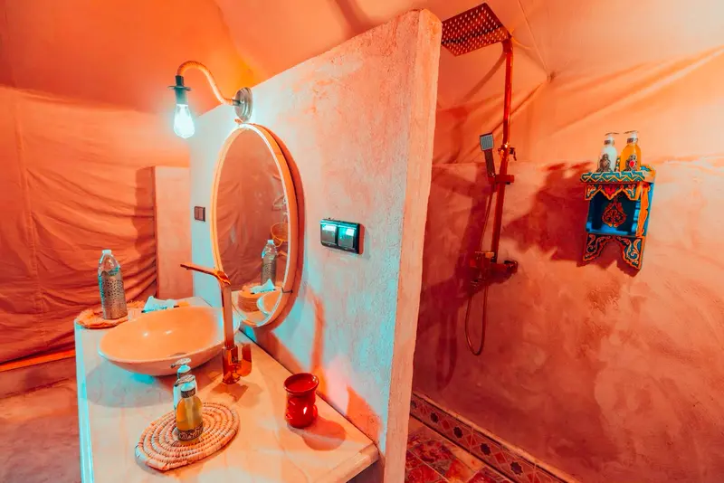 Doccia a pioggia nel bagno privato della tenda, accanto al lavabo in pietra e allo specchio rotondo