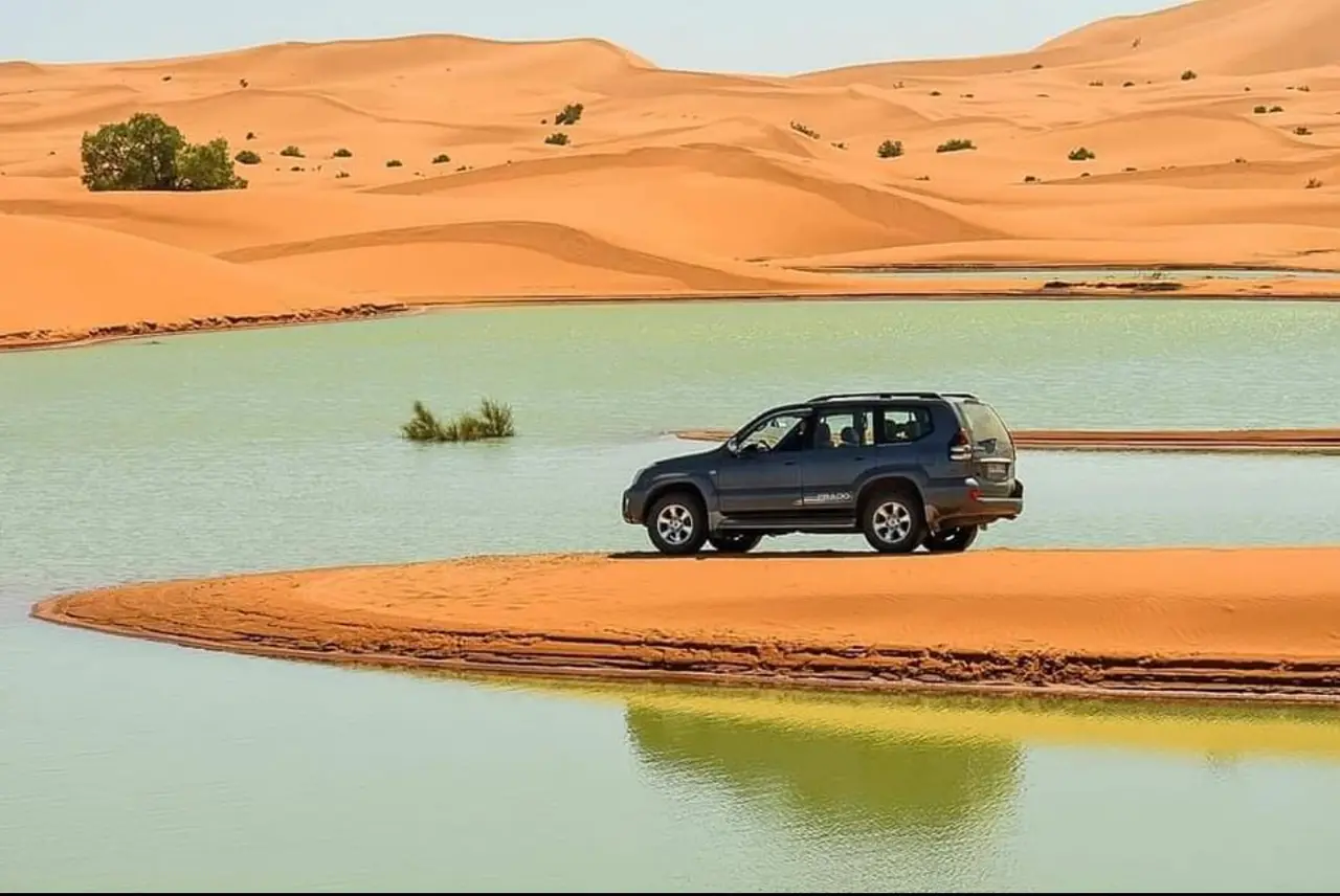 4x4 vehicle beside a water-filled oasis in the Merzouga desert