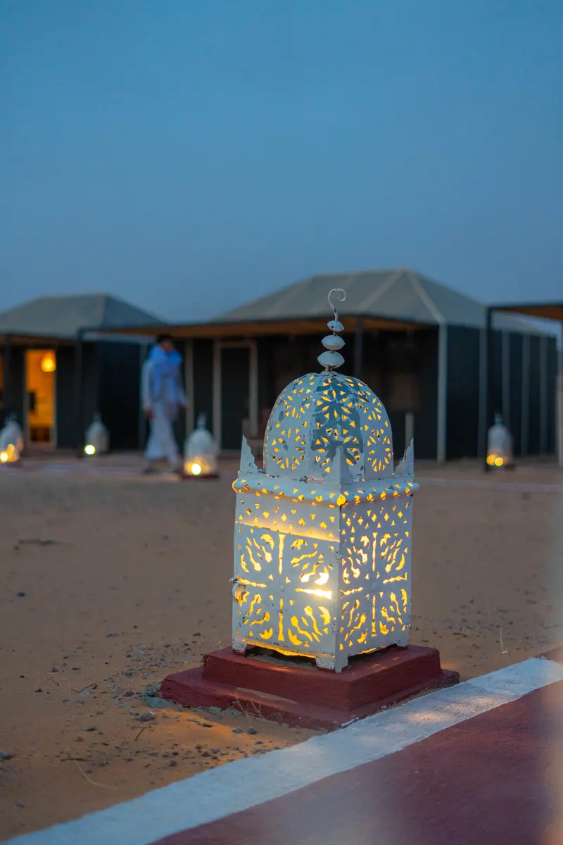 Moroccan lantern lit, marking the path between the tents at the camp