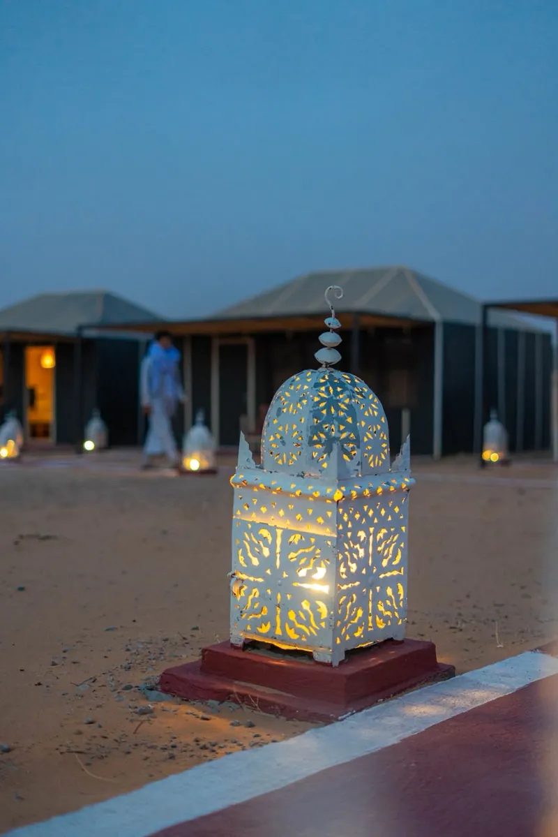 Lit Moroccan lantern at dusk on the path between the tents