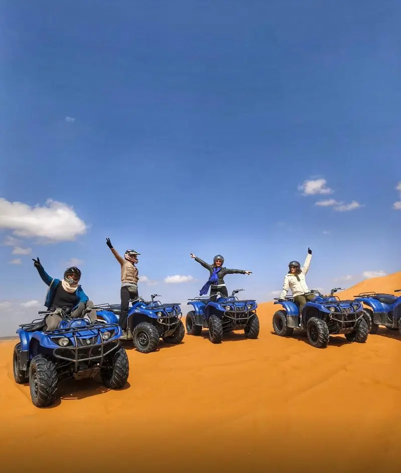 Un groupe d’hôtes casqués posant sur leurs quads dans les dunes de Merzouga