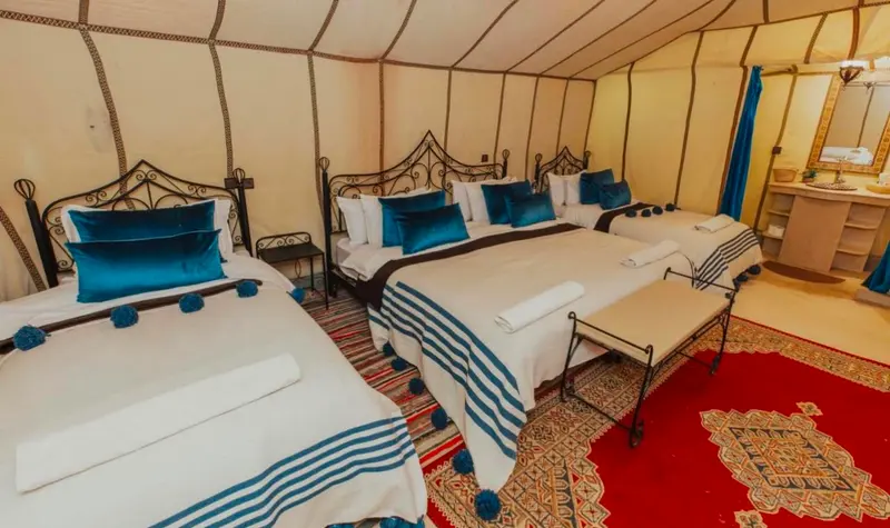 Tenda quadrupla con letti in ferro battuto, cuscini blu e tappeto marocchino rosso