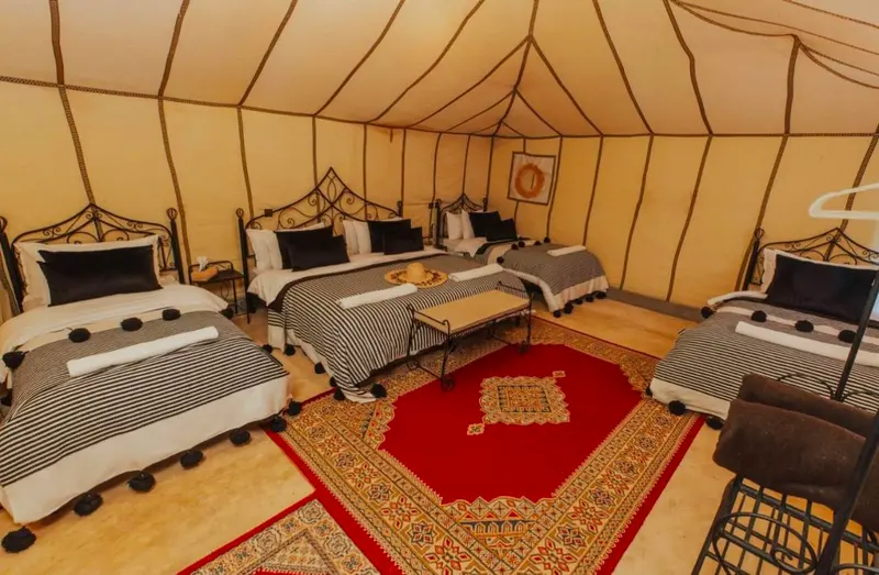 Tenda familiare con quattro letti in ferro battuto, coperte a righe e tappeto marocchino rosso