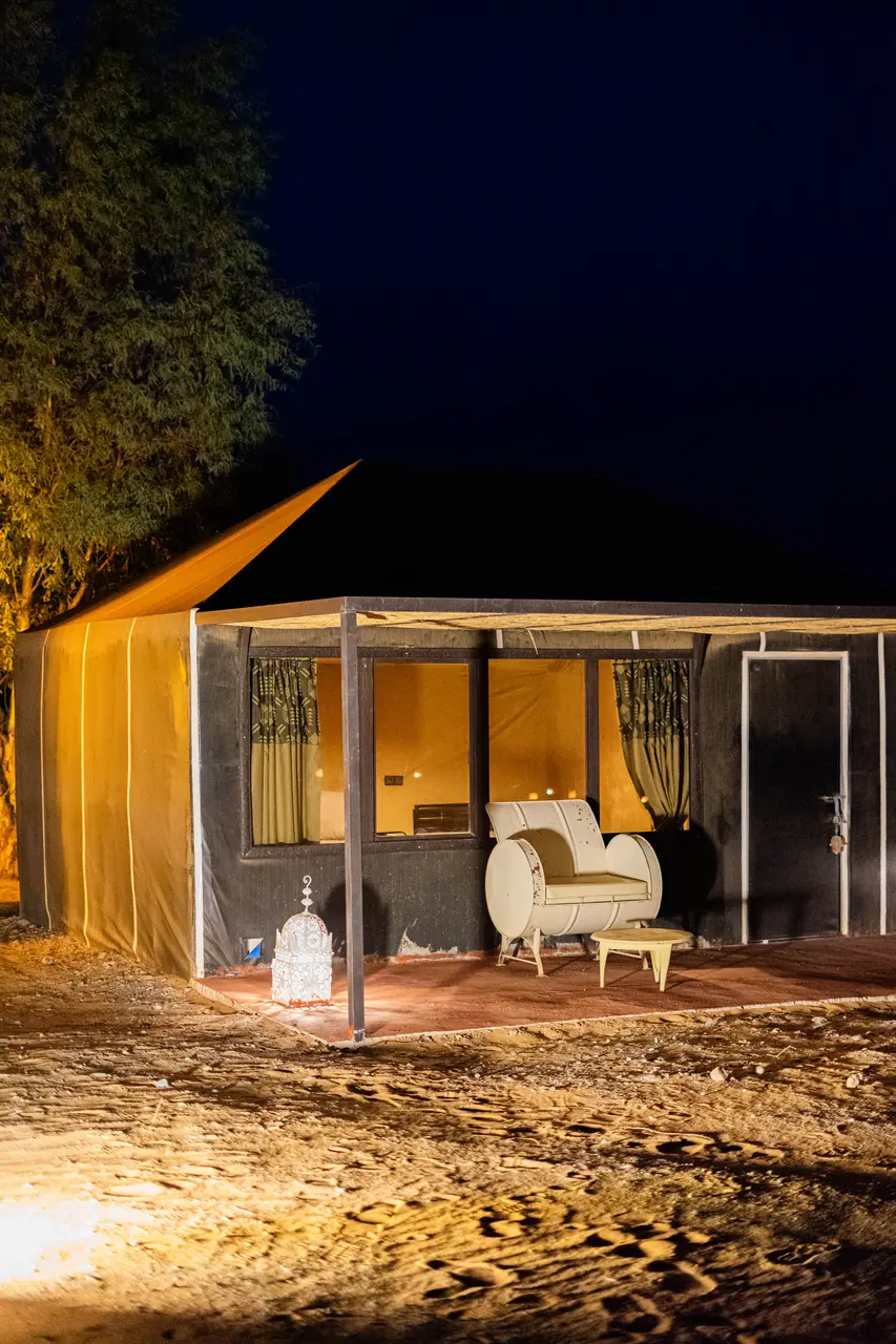 Jaima iluminada de noche vista desde fuera, con el sillón en la terraza