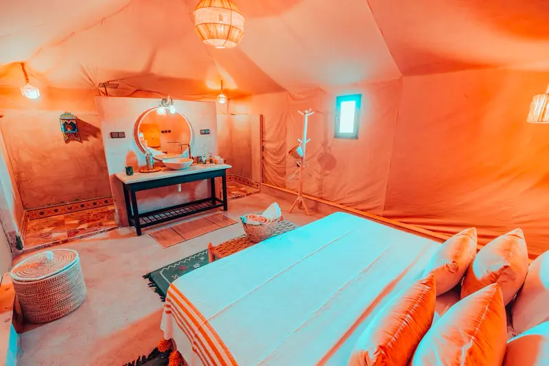 Tenda singola con letto grande, cuscini color senape e il lavabo con specchio rotondo sul fondo