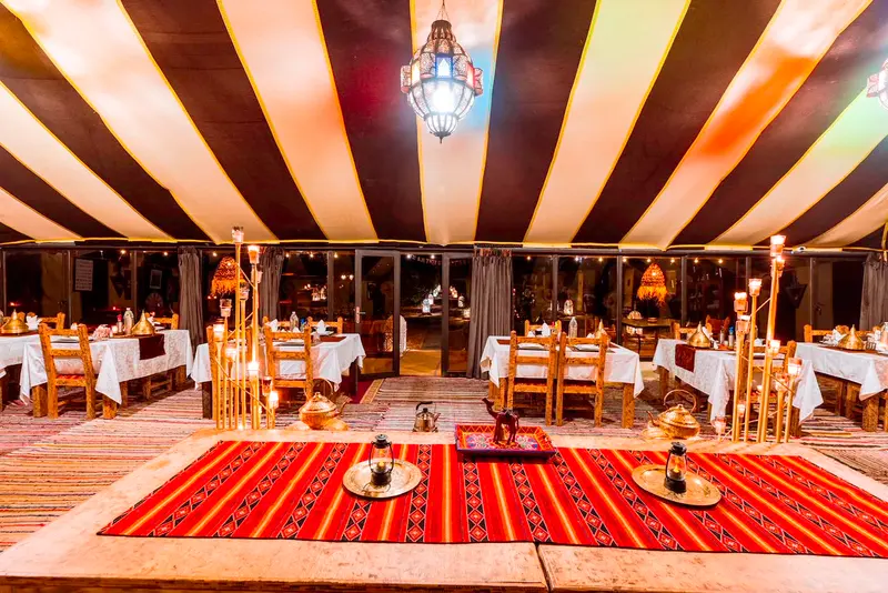 La tenda ristorante di sera, con i tavoli apparecchiati, candelabri e una lanterna marocchina appesa al soffitto