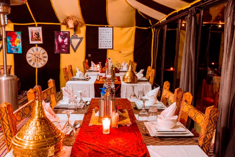 Lunga tavola apparecchiata per la cena nella tenda ristorante, con tajine di ottone e candele
