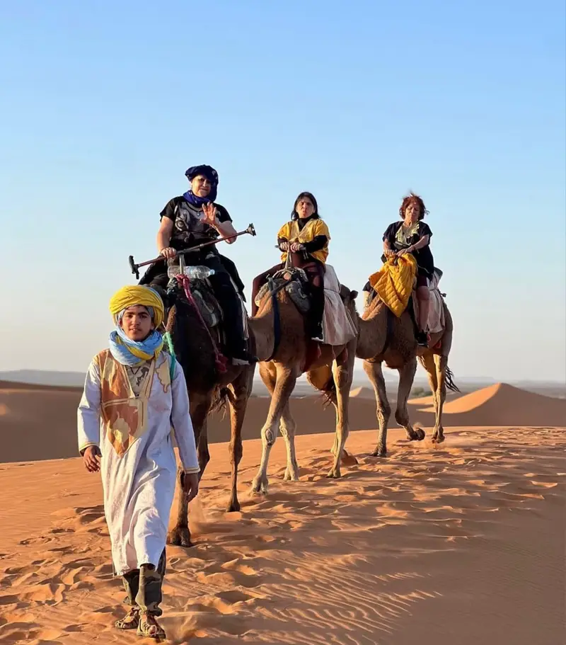 Guests riding camels with a Berber guide on the Merzouga dunes