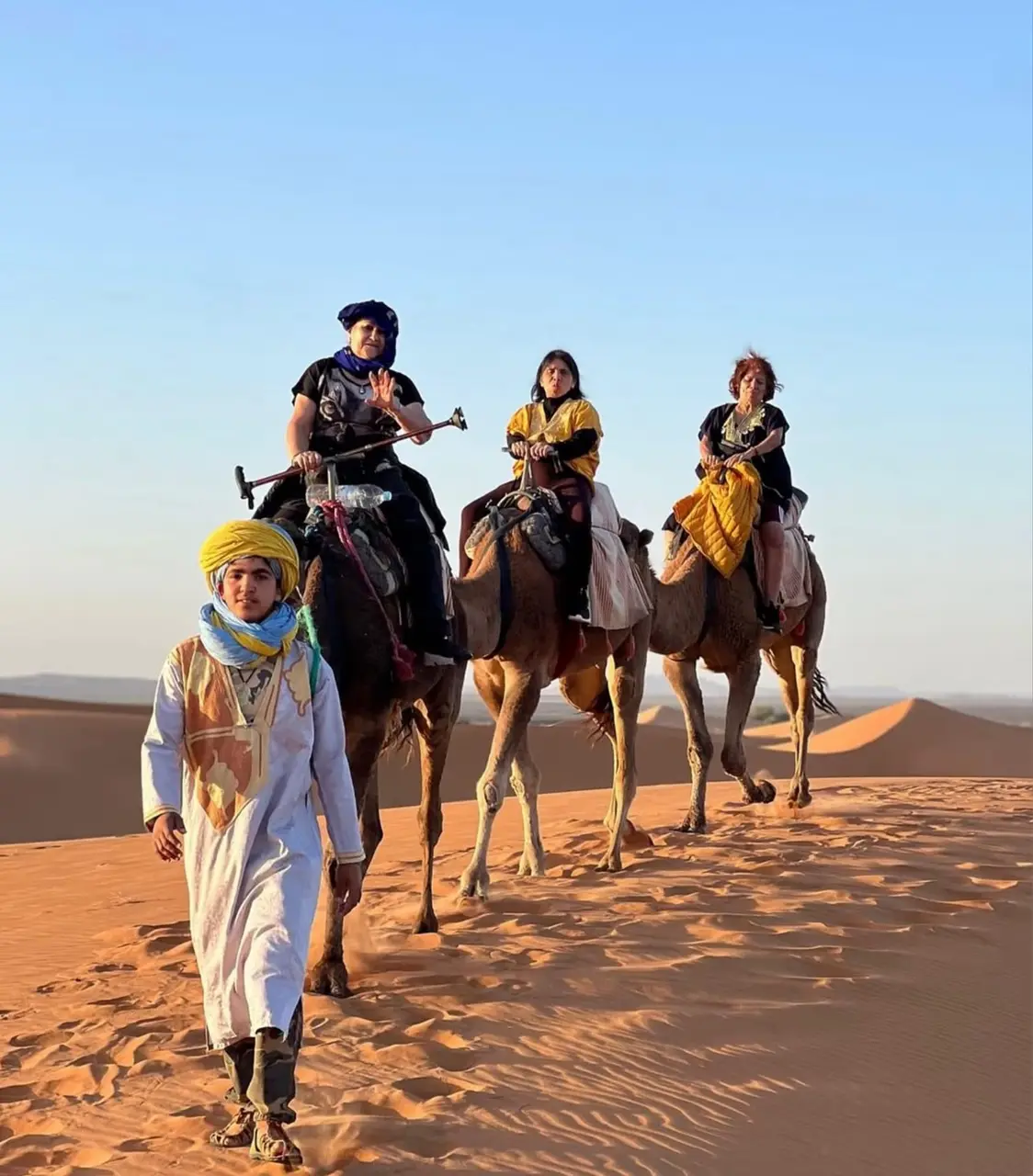 Huéspedes montando en dromedario acompañados por un guía bereber en las dunas de Merzouga