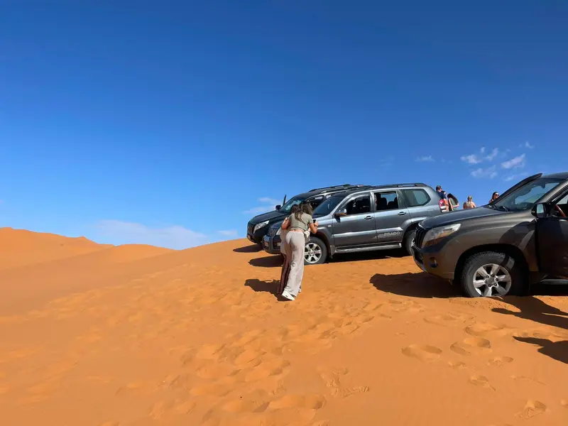Plusieurs 4x4 en haut d’une dune, avec des hôtes descendant sur le sable